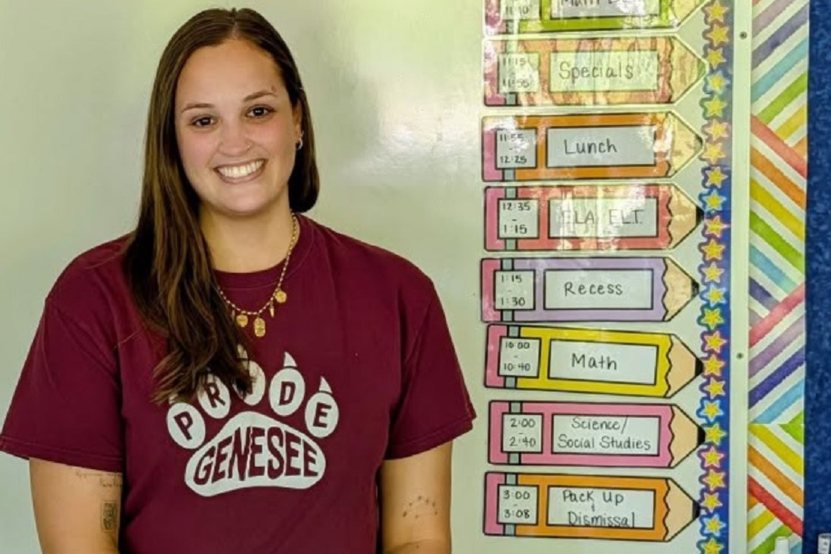 Smiling female student in a maroon shirt standing next to a colorful classroom schedule display showing periods like Lunch and Math.