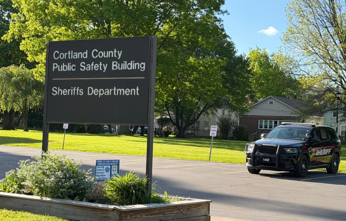 Large sign reads 'Cortland County Public Safety Building' with 'Sheriffs Department' beneath; a sheriff SUV parked nearby on a sunny day.