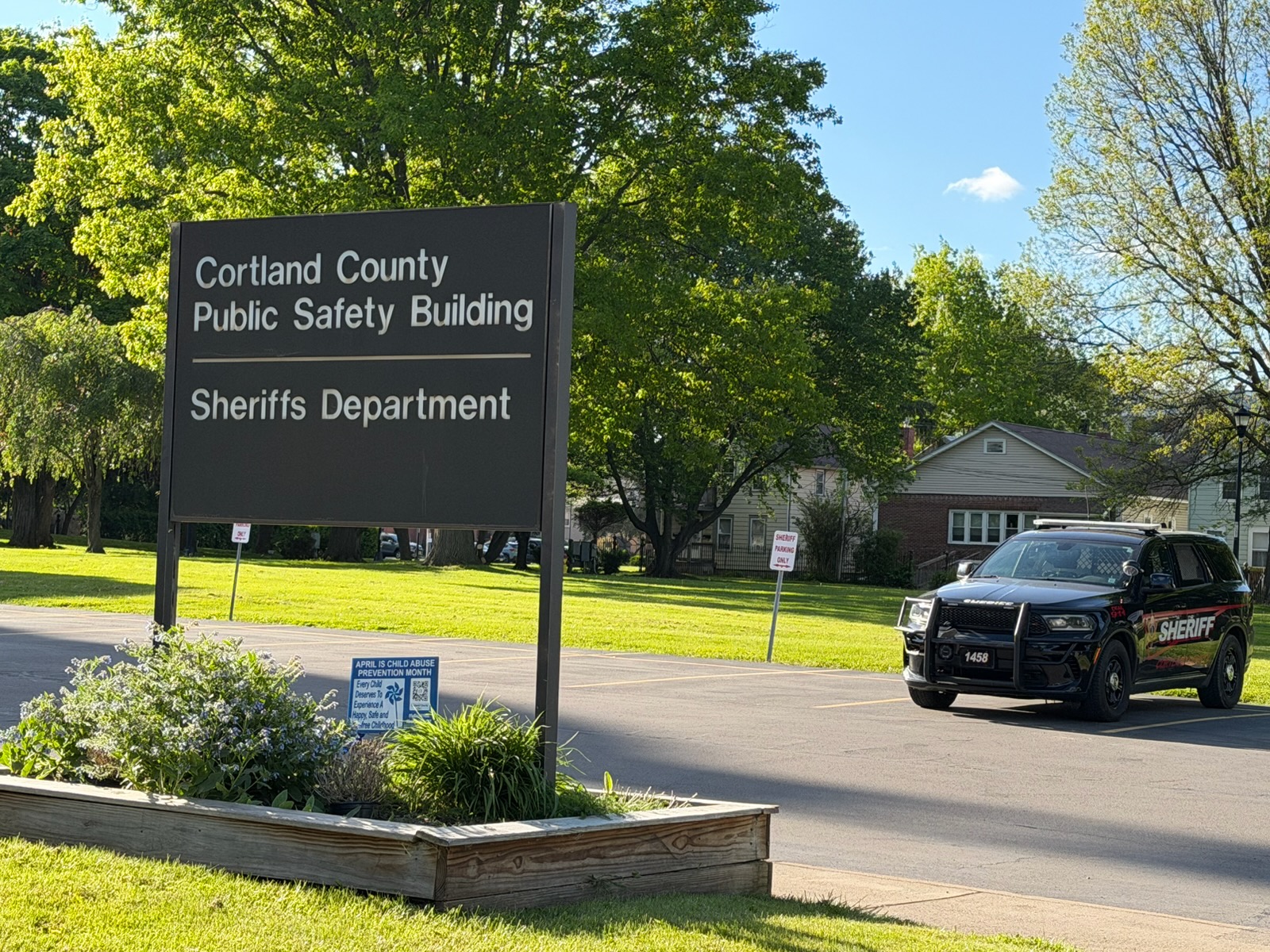 Large sign reads 'Cortland County Public Safety Building' with 'Sheriffs Department' beneath; a sheriff SUV parked nearby on a sunny day.