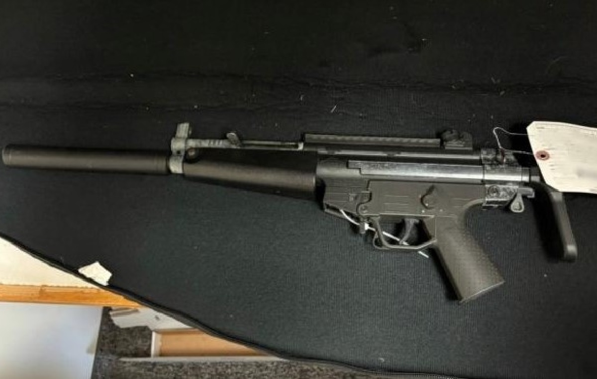 Long-barreled rifle with a suppressor resting on a dark surface, left side visible.