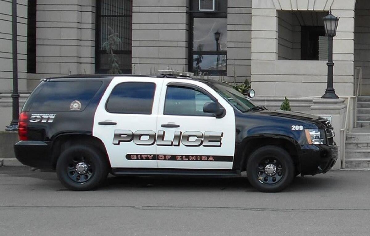 Police SUV parked on a city street in front of a stone government building; POLICE and City of Elmira markings on the side.