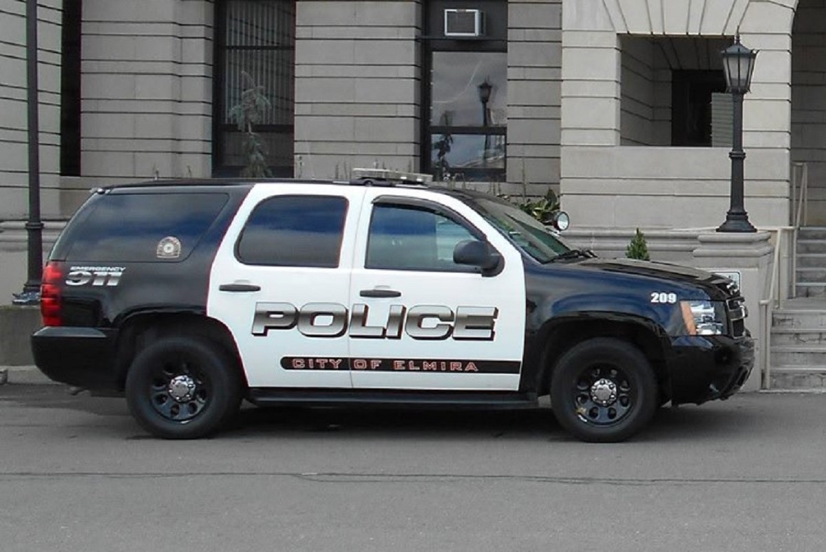 Police SUV parked on a city street in front of a stone government building; POLICE and City of Elmira markings on the side.