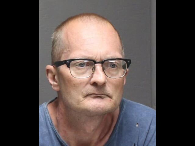Mugshot of a middle-aged man with glasses, wearing a blue shirt, looking slightly to the left with a neutral expression.