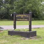 Wooden sign for W.B. Strong Fire Co. Inc. and Freeville Fire Dept. with gold lettering, set in a grassy area with trees behind.