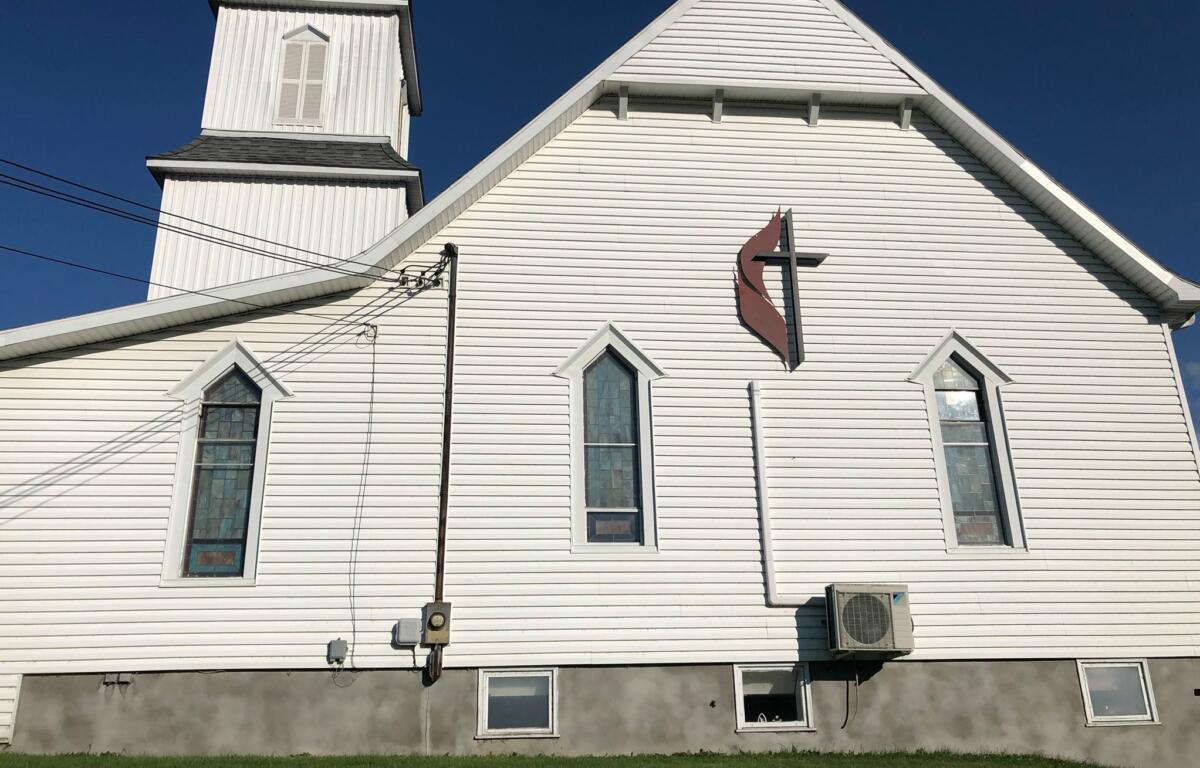 White wooden church facade with steep gables, tall arched windows, and a red abstract wall sign against a clear blue sky.