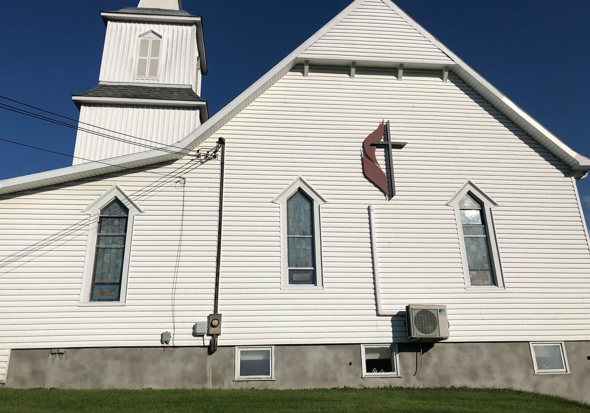 White wooden church facade with steep gables, tall arched windows, and a red abstract wall sign against a clear blue sky.