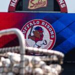 Scoreboard displaying the Buffalo Bisons logo in a red‑to‑blue gradient background; blurred stadium equipment in the foreground.