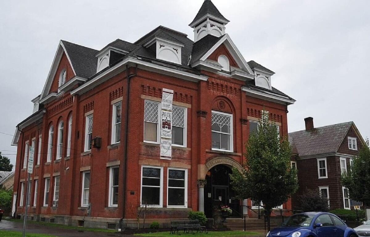 Red brick town-style building with white trim, arched windows, and a small cupola on a rainy street.