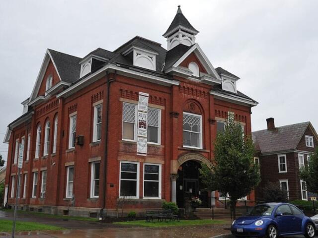 Red brick town-style building with white trim, arched windows, and a small cupola on a rainy street.