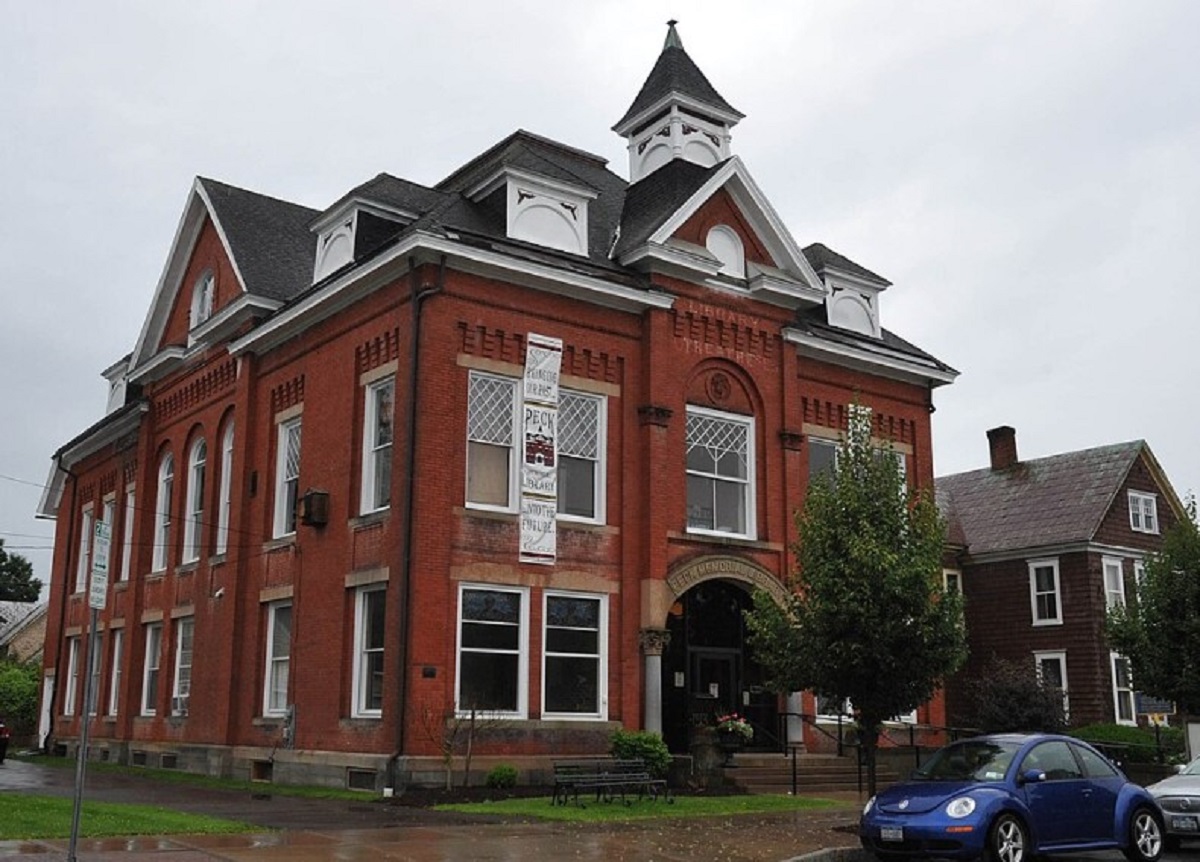 Red brick town-style building with white trim, arched windows, and a small cupola on a rainy street.