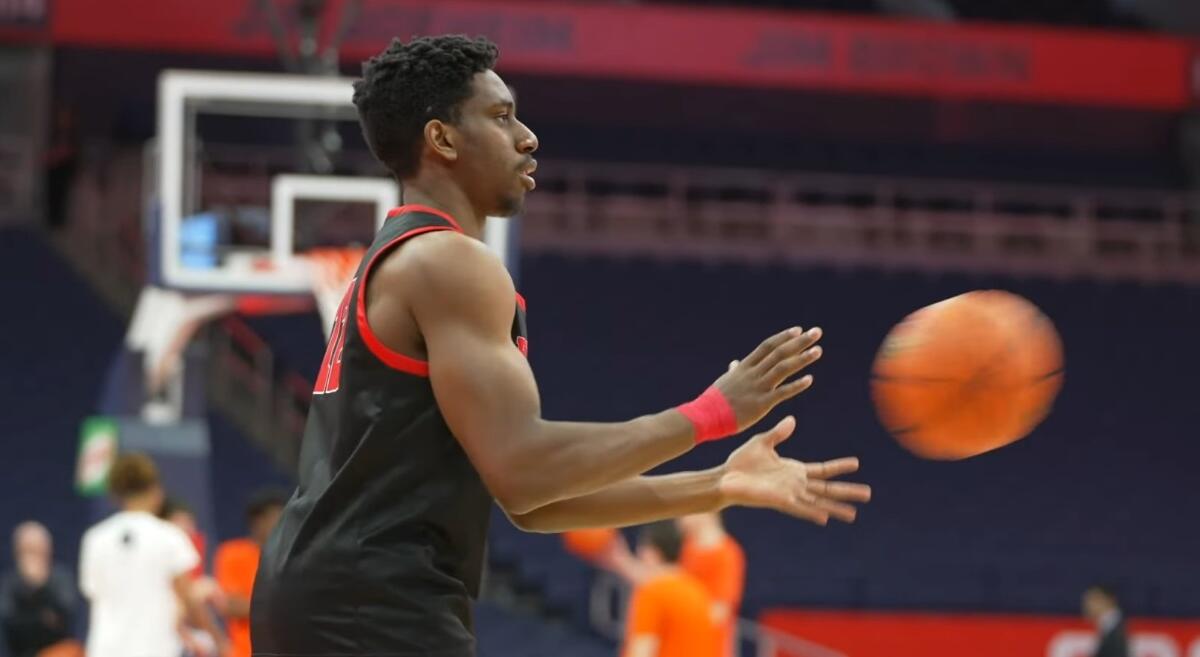 Basketball player in a black uniform passing an orange ball on a court with spectators in the background.