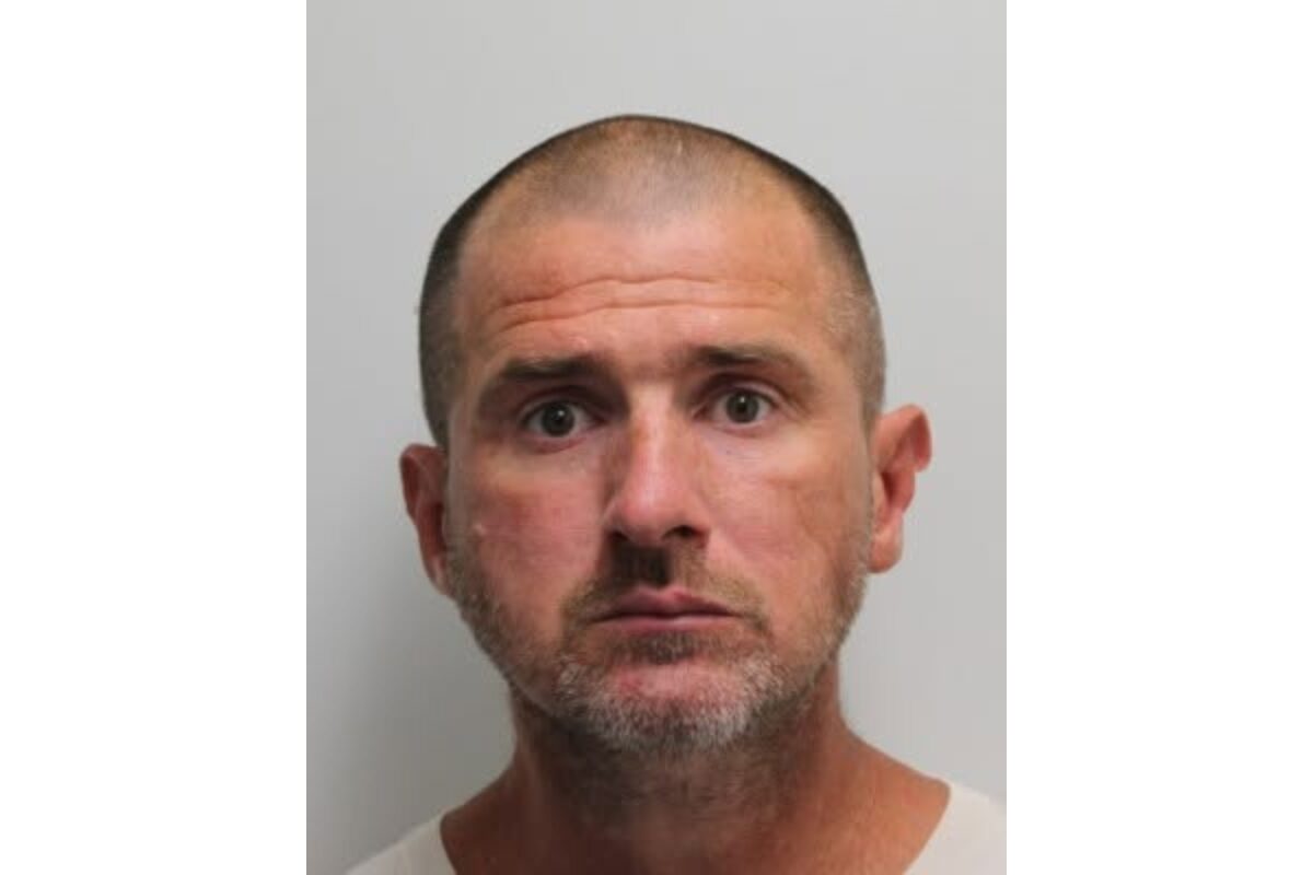 Mugshot of a middle-aged man with short hair and stubble, wearing a white shirt against a gray background.