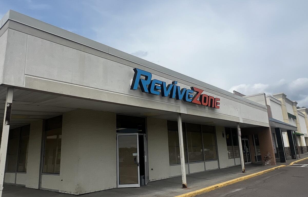 Storefront of a strip mall with a blue and red 'ReviveZone' sign above the entrance, under a pale blue sky