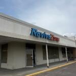 Storefront of a strip mall with a blue and red 'ReviveZone' sign above the entrance, under a pale blue sky