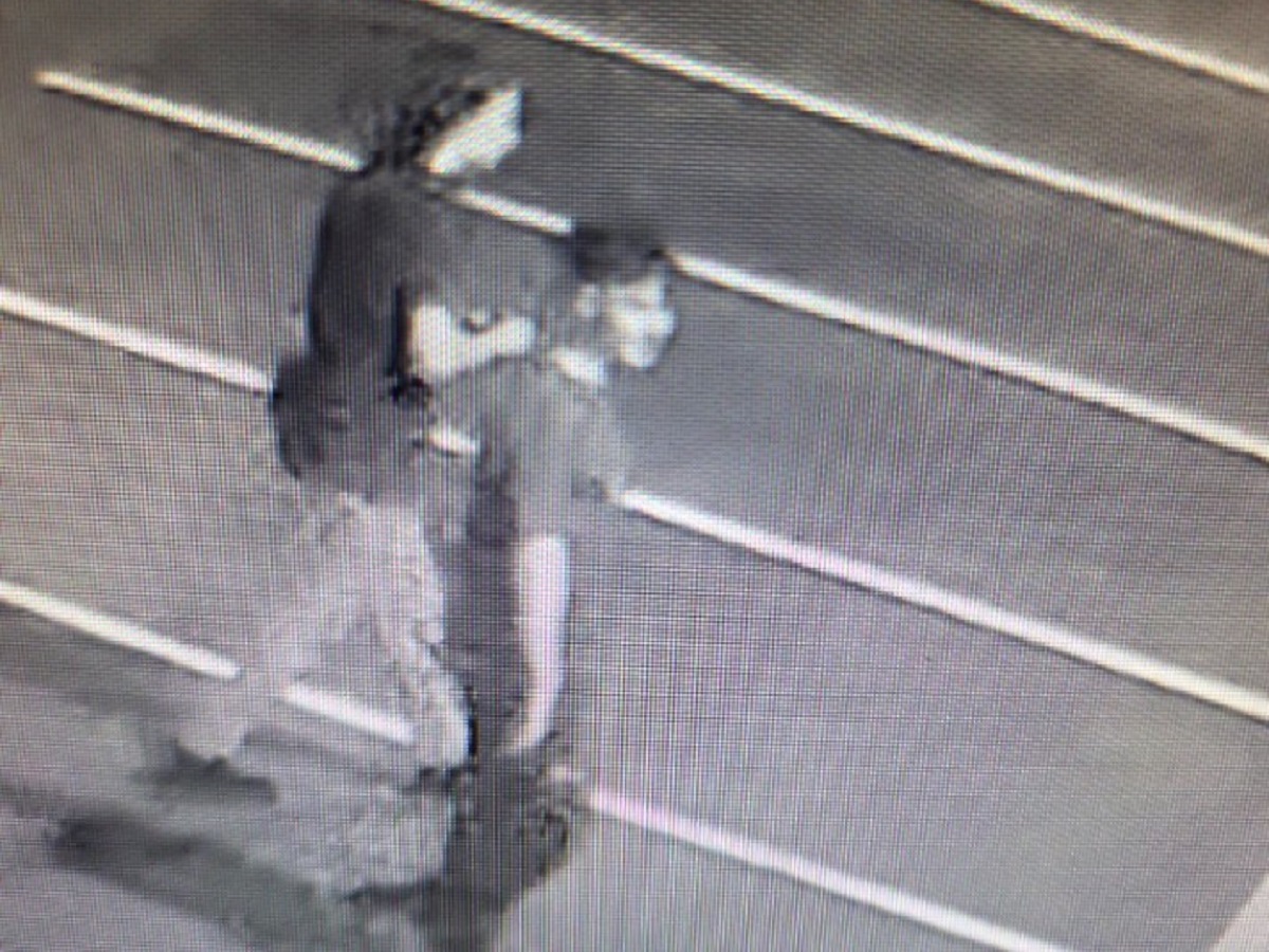 Grainy security image of an adult in dark clothing standing over a smaller person on a street at night.