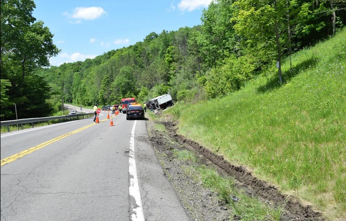 Two-lane rural road scene with a truck off the embankment, emergency vehicles and orange cones blocking the lane during a crash response.