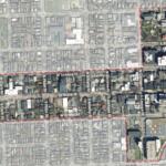 Aerial view of a city grid with a red dashed boundary outlining a district, showing labeled streets and dense blocks.