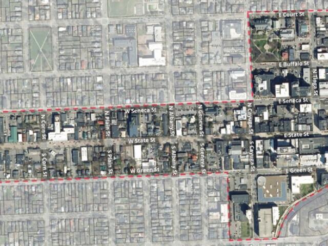 Aerial view of a city grid with a red dashed boundary outlining a district, showing labeled streets and dense blocks.