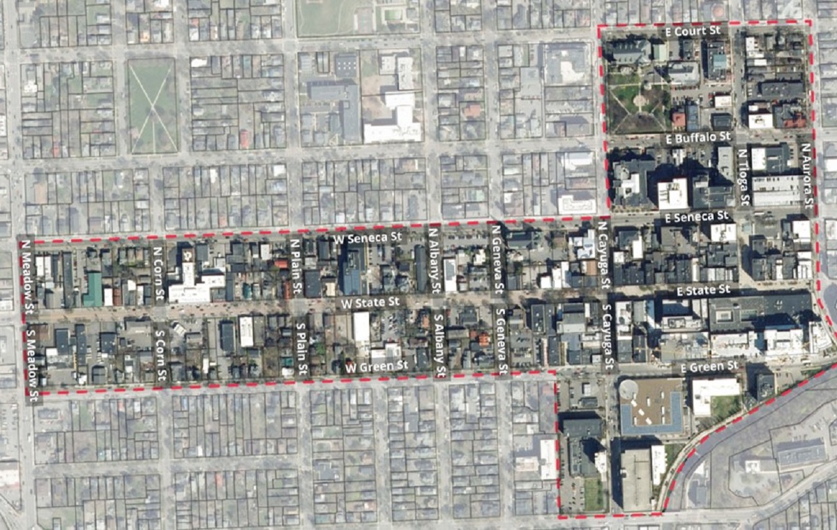 Aerial view of a city grid with a red dashed boundary outlining a district, showing labeled streets and dense blocks.