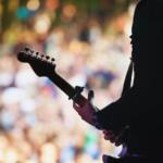 Guitarist performing on stage in front of a crowd silhouette