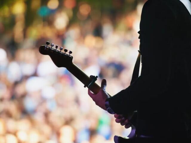 Guitarist performing on stage in front of a crowd silhouette