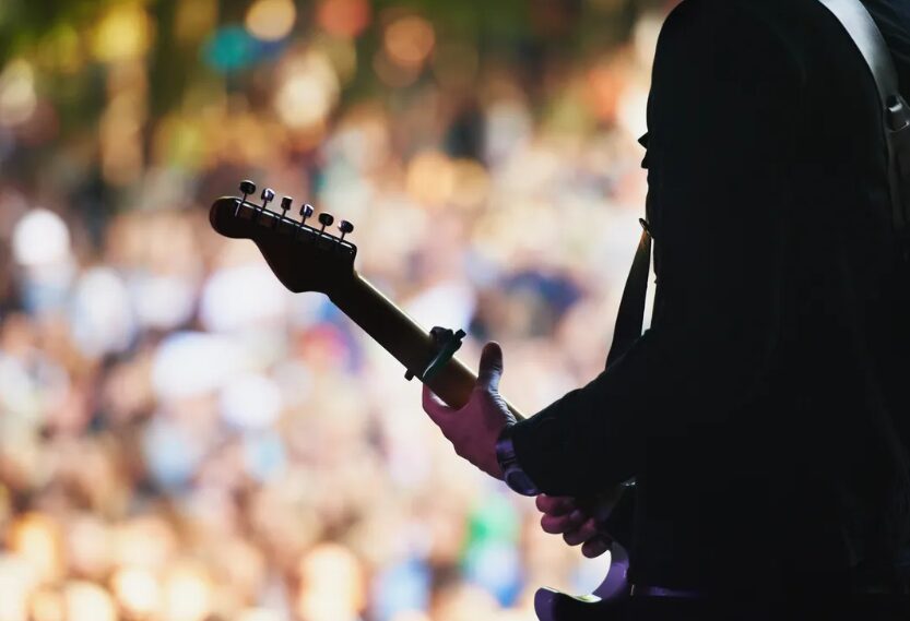Guitarist performing on stage in front of a crowd silhouette