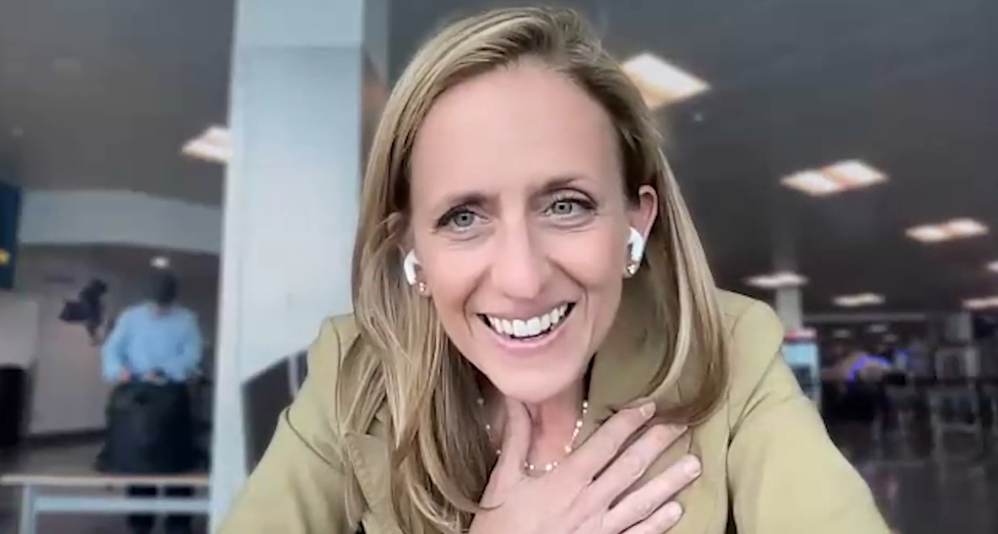 Smiling woman with blond hair wearing wireless earbuds during a video call in an office setting.