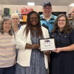 Group of adults posing in a store, smiling and holding a framed certificate that reads 'Area 51.'