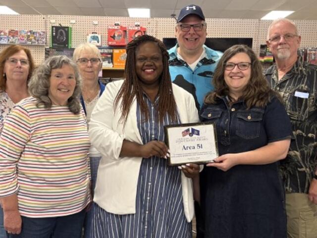 Group of adults posing in a store, smiling and holding a framed certificate that reads 'Area 51.'