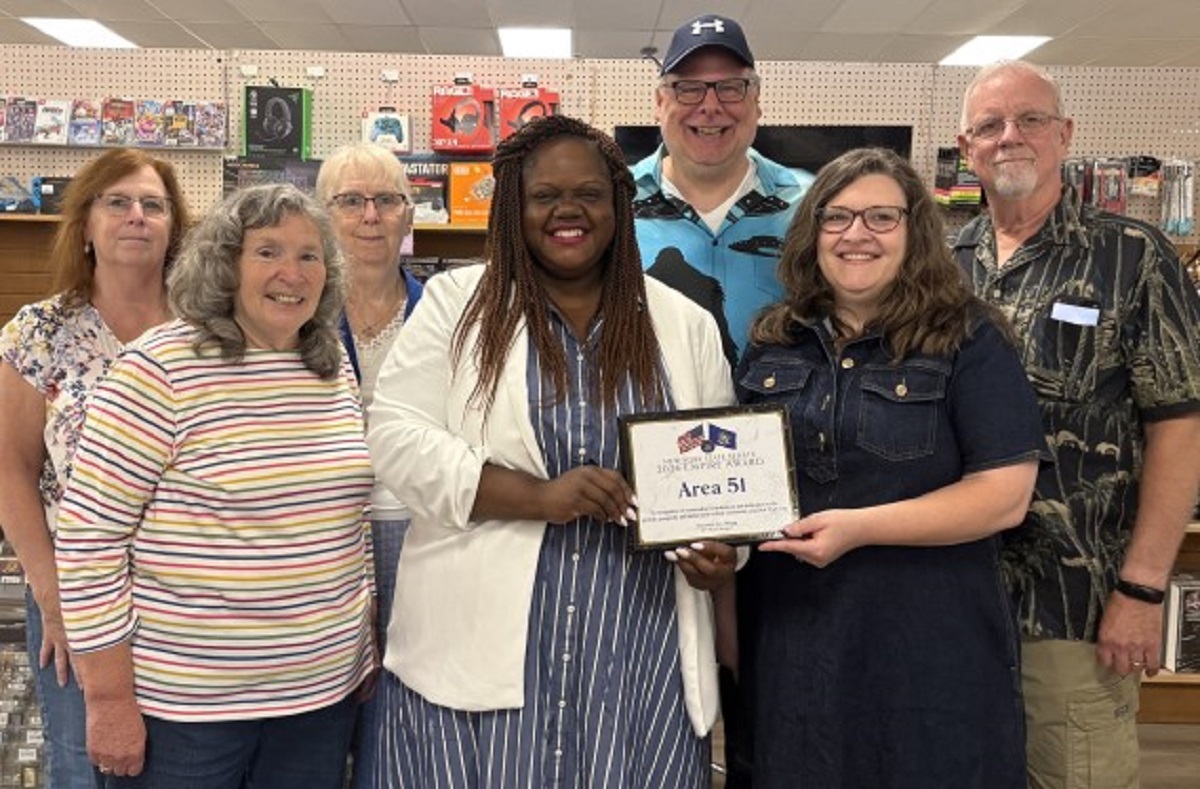 Group of adults posing in a store, smiling and holding a framed certificate that reads 'Area 51.'