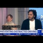 Two interview guests sit in a TV studio discussing distracted driving; on-screen headline reads 'PREVENTING DISTRACTED DRIVING'.