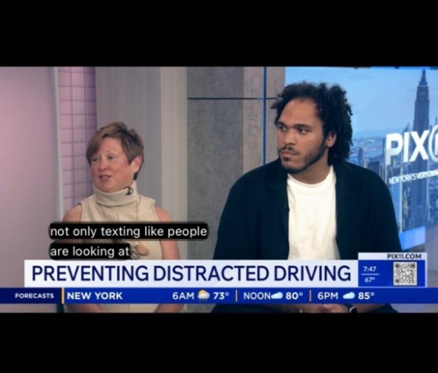 Two interview guests sit in a TV studio discussing distracted driving; on-screen headline reads 'PREVENTING DISTRACTED DRIVING'.