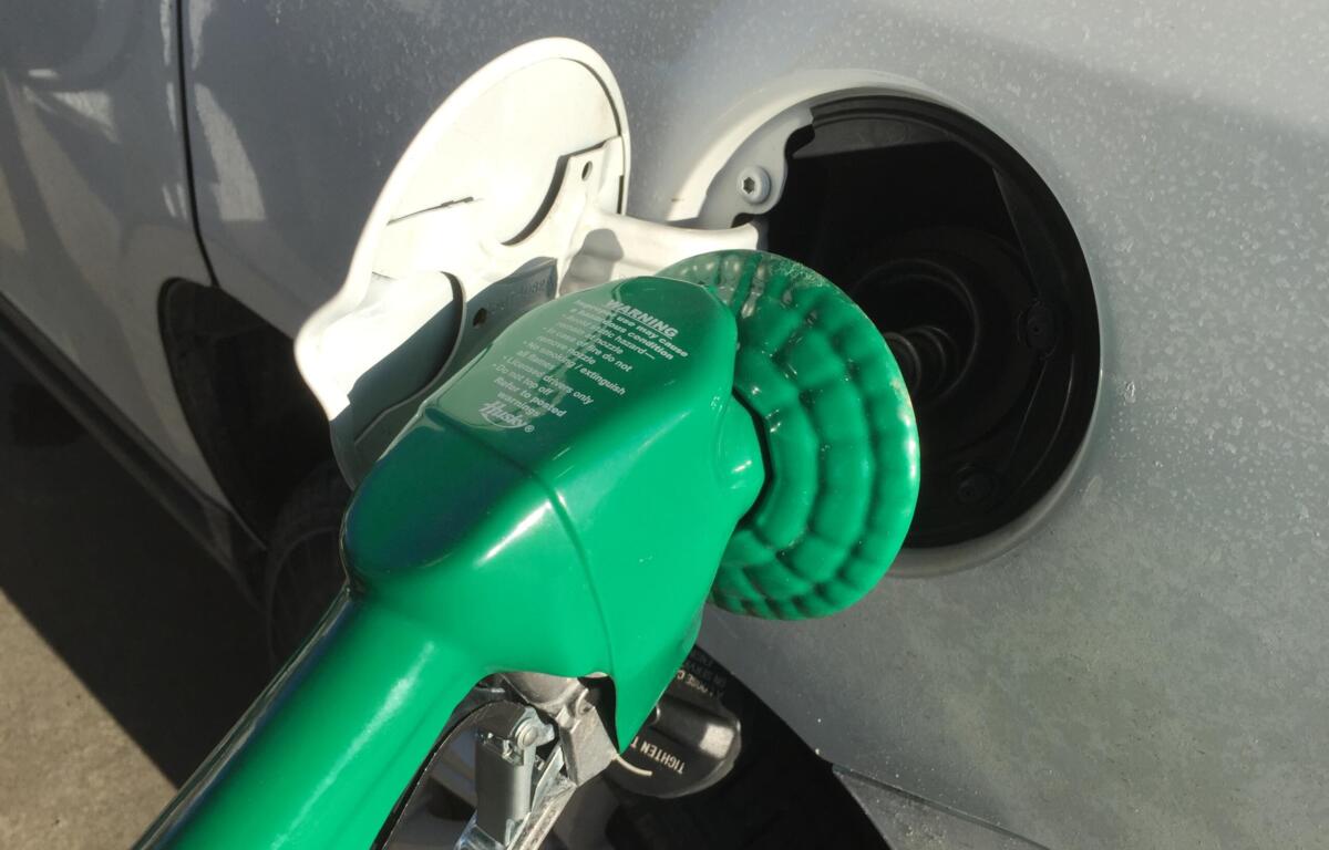 Open fuel door on a gray car with a green gas cap attached by a tether.