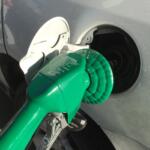 Open fuel door on a gray car with a green gas cap attached by a tether.