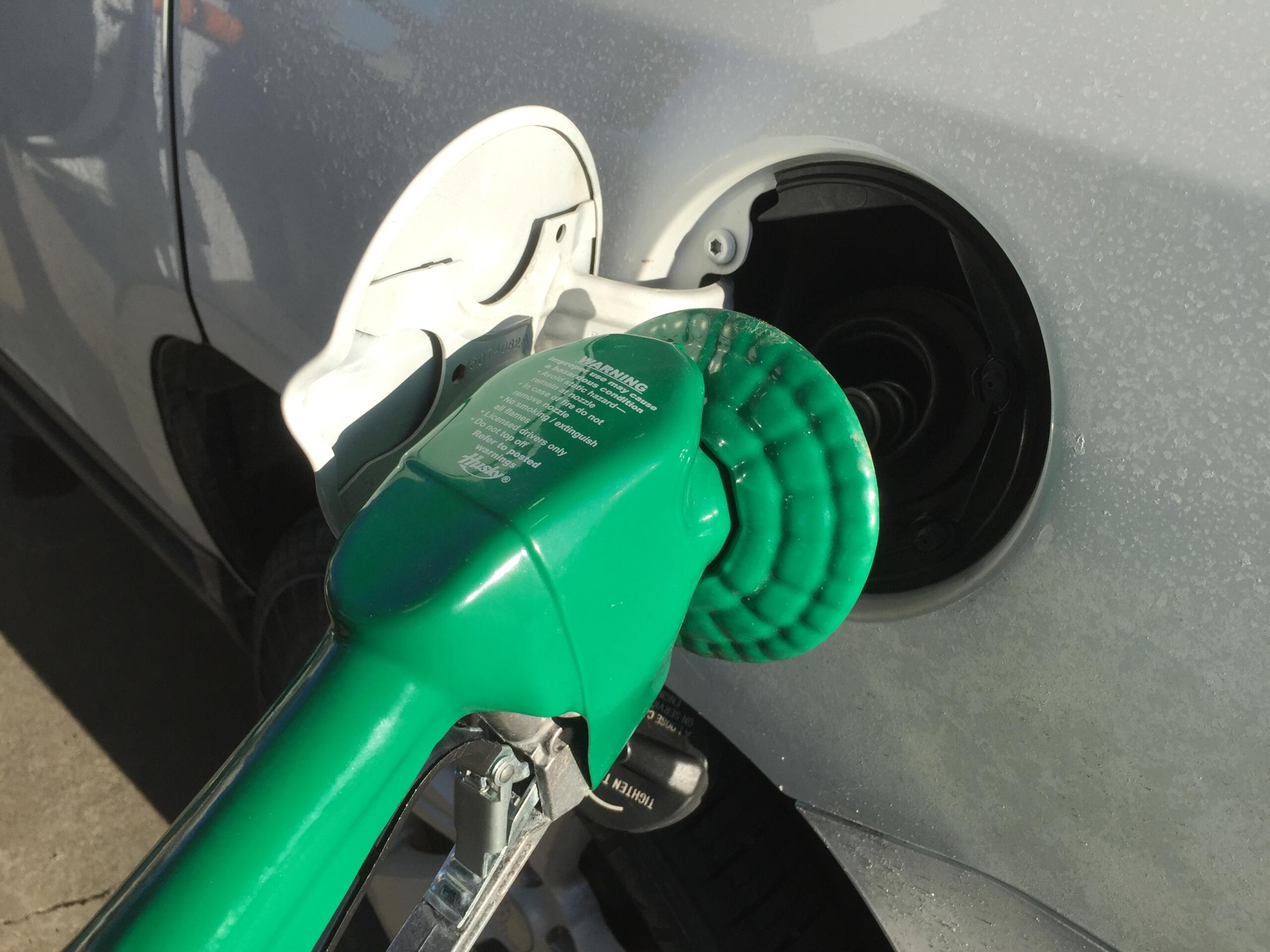Open fuel door on a gray car with a green gas cap attached by a tether.
