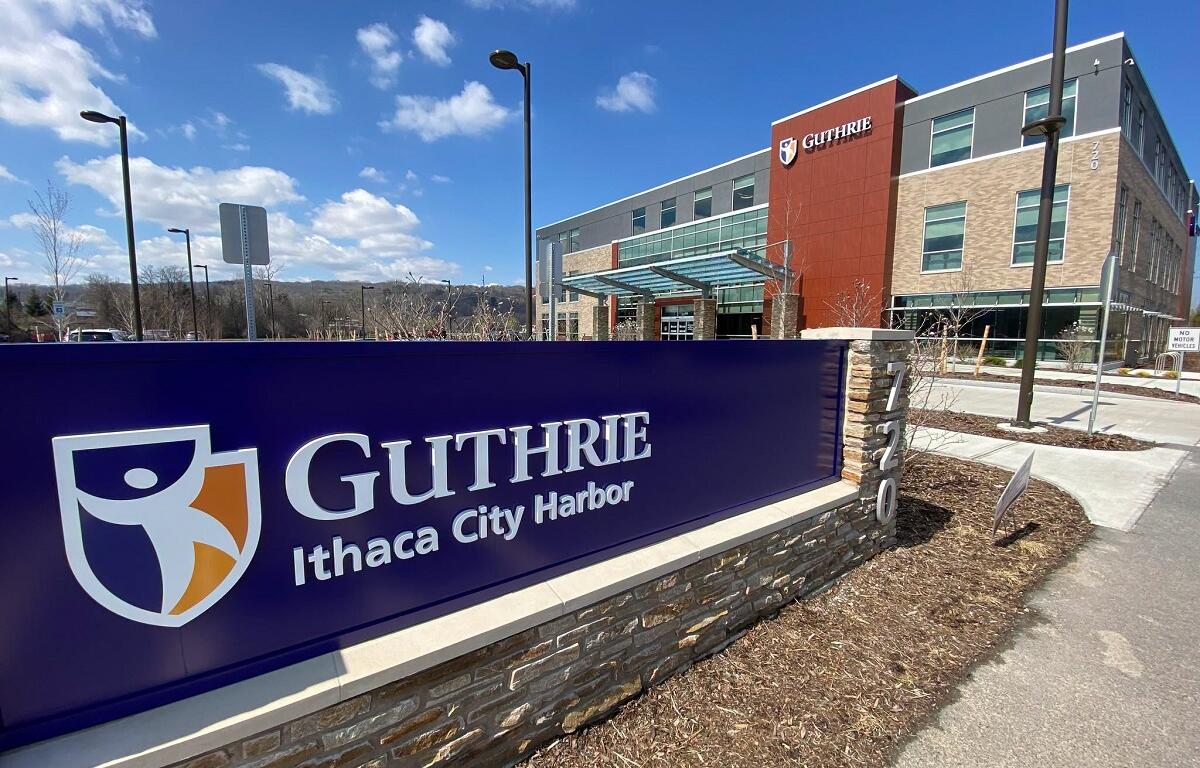 Front sign for Guthrie Ithaca City Harbor with a modern medical campus building in the background under a blue sky.
