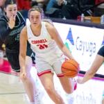 Cornell player wearing number 31 in white dribbles the ball while defended by two opponents in green jerseys on a basketball court.