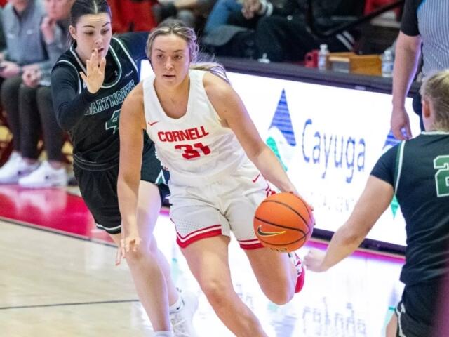 Cornell player wearing number 31 in white dribbles the ball while defended by two opponents in green jerseys on a basketball court.