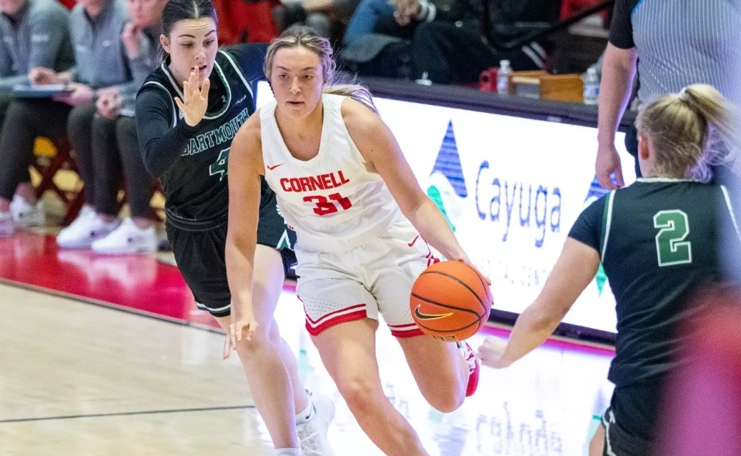 Cornell player wearing number 31 in white dribbles the ball while defended by two opponents in green jerseys on a basketball court.