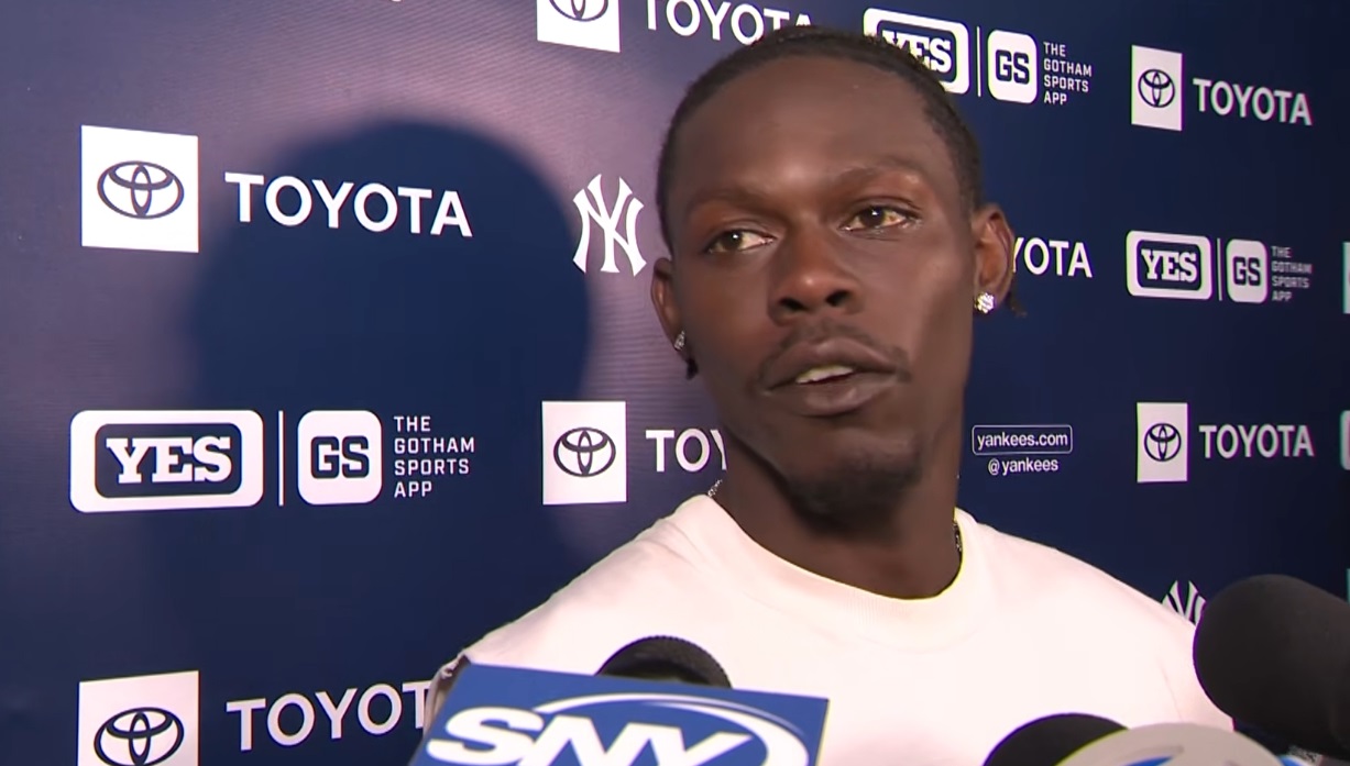 Athlete being interviewed at a press backdrop with Yankees and Toyota logos; several microphones in front.