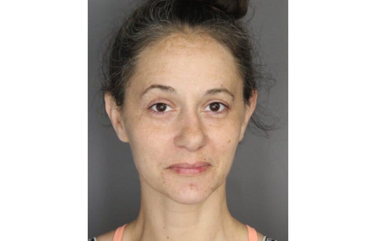 Front-facing head-and-shoulders portrait of a woman with light skin, dark hair in a messy bun, neutral expression and visible facial redness/acne.
