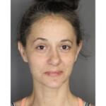 Front-facing head-and-shoulders portrait of a woman with light skin, dark hair in a messy bun, neutral expression and visible facial redness/acne.