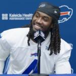Bills player at a press conference, smiling into a microphone with a blue backdrop featuring Kaleida Health logos.