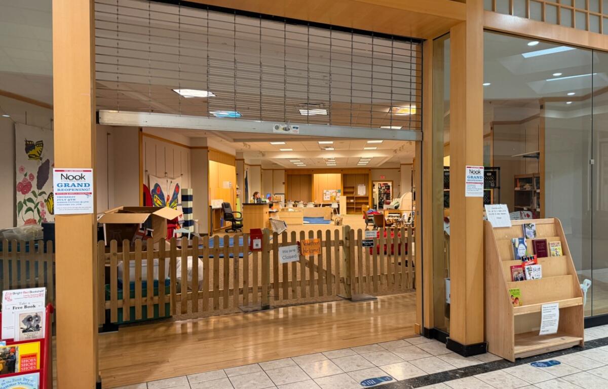 Store interior with a wooden fence and open space, shelves and a sign announcing Nook grand reopening.