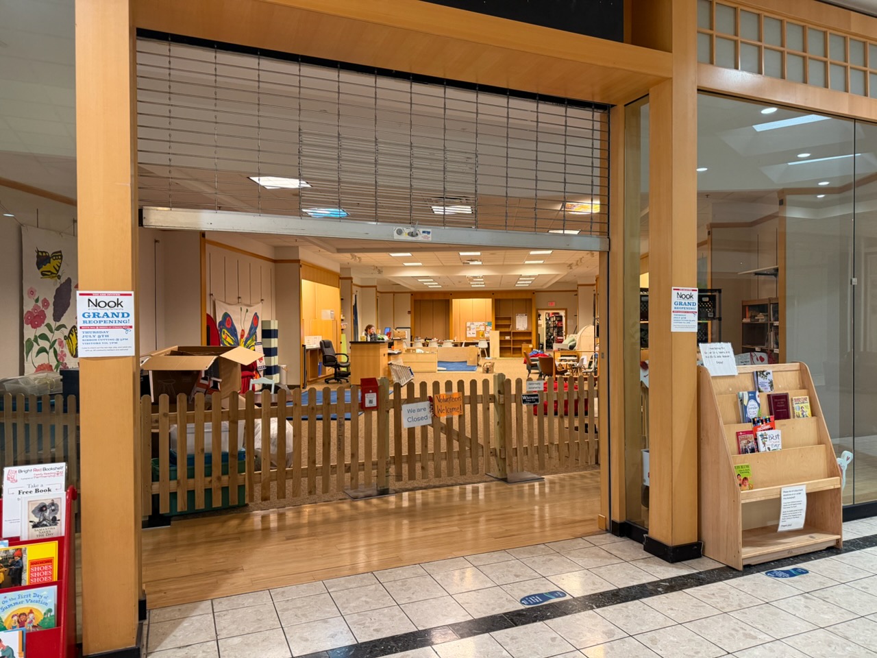 Store interior with a wooden fence and open space, shelves and a sign announcing Nook grand reopening.