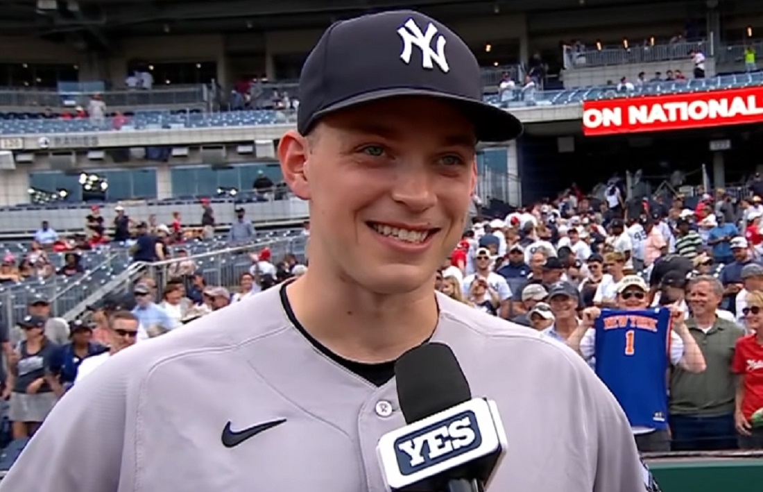 Baseball player in Yankees cap being interviewed on the field with a YES microphone; stadium crowd in the background.