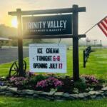 Sign for Trinity Valley Creamery & Market with a marquee announcing ice cream tonight 6–8 and July 17 opening, beside an American flag.