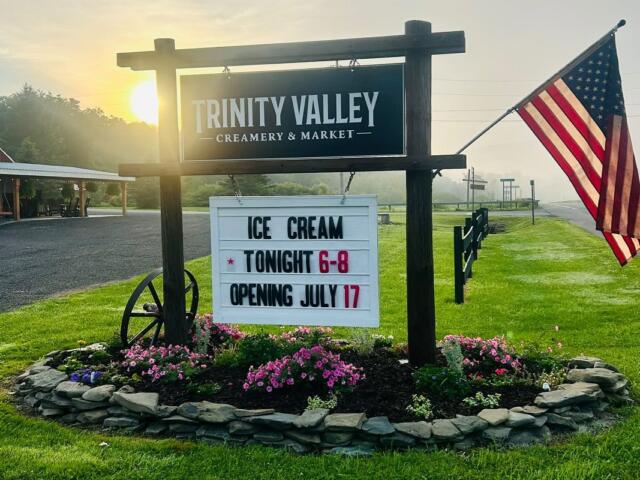 Sign for Trinity Valley Creamery & Market with a marquee announcing ice cream tonight 6–8 and July 17 opening, beside an American flag.