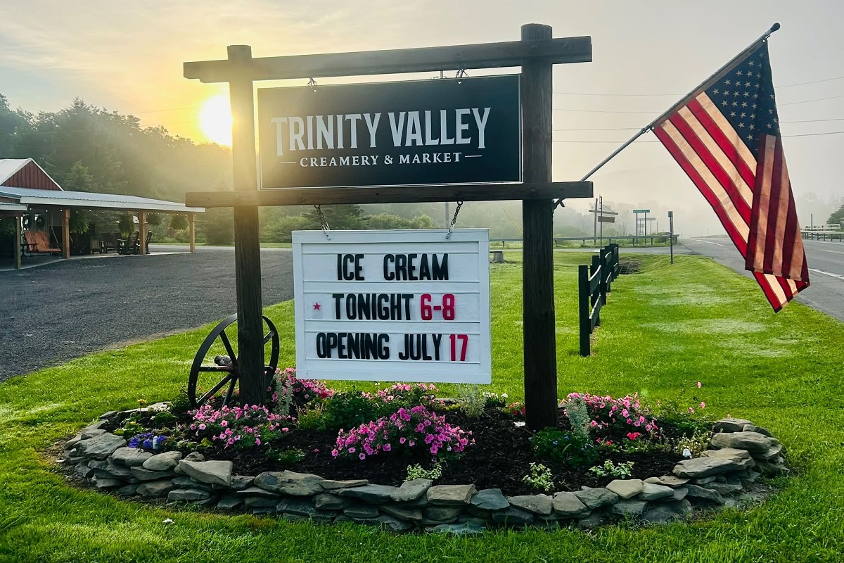 Sign for Trinity Valley Creamery & Market with a marquee announcing ice cream tonight 6–8 and July 17 opening, beside an American flag.