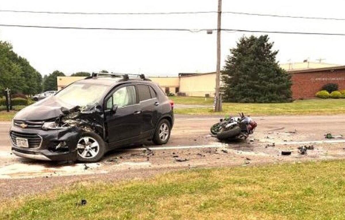 Black SUV with severe front-end damage after a collision on a road, debris scattered across the street, and a toppled motorcycle nearby.